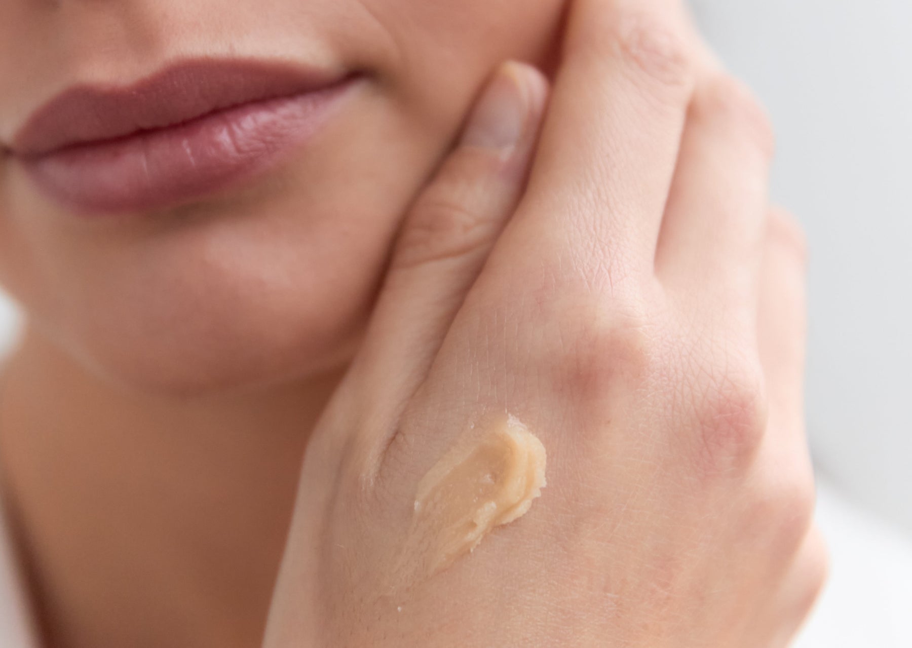 Frau berührt Gesicht mit Creme auf Handrücken